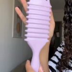 Light purple wide-tooth comb held by a person with curly dark hair.