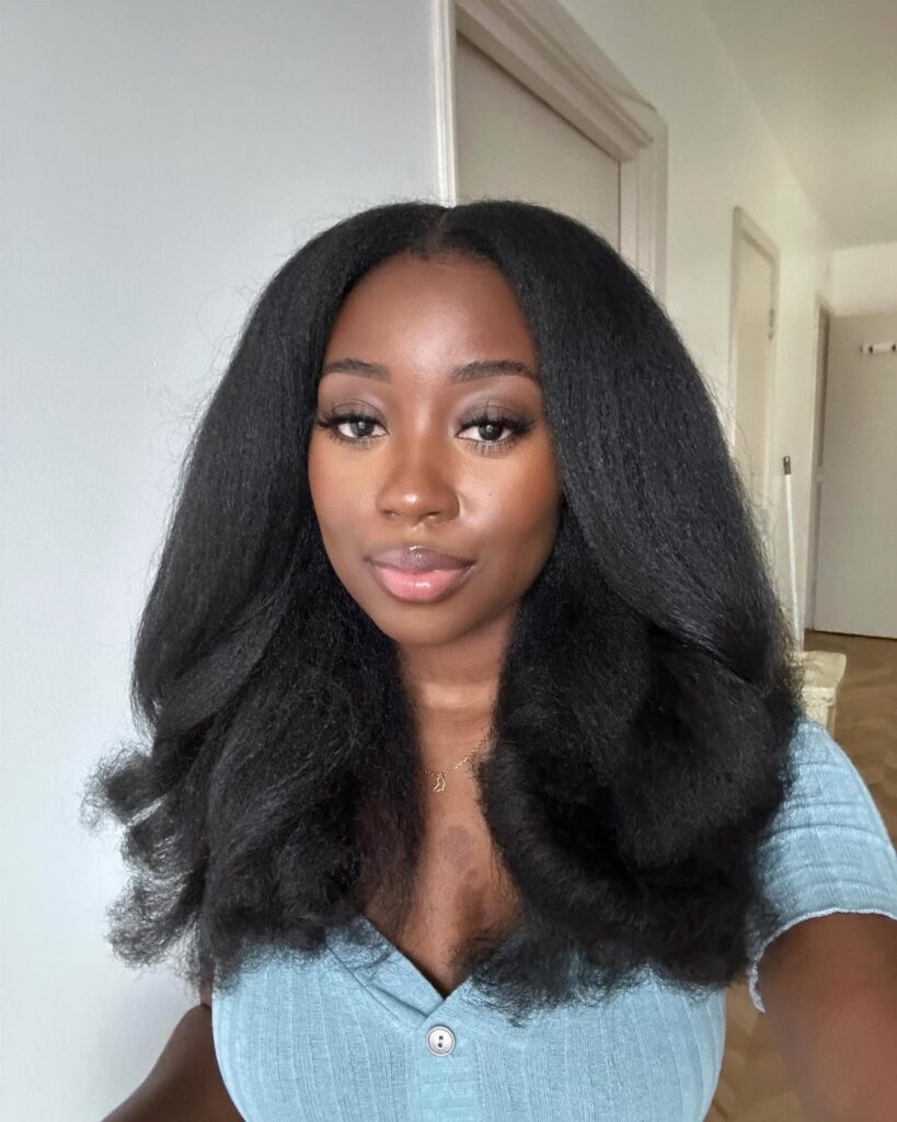 Woman with voluminous long black afro hair wearing a light blue ribbed top.