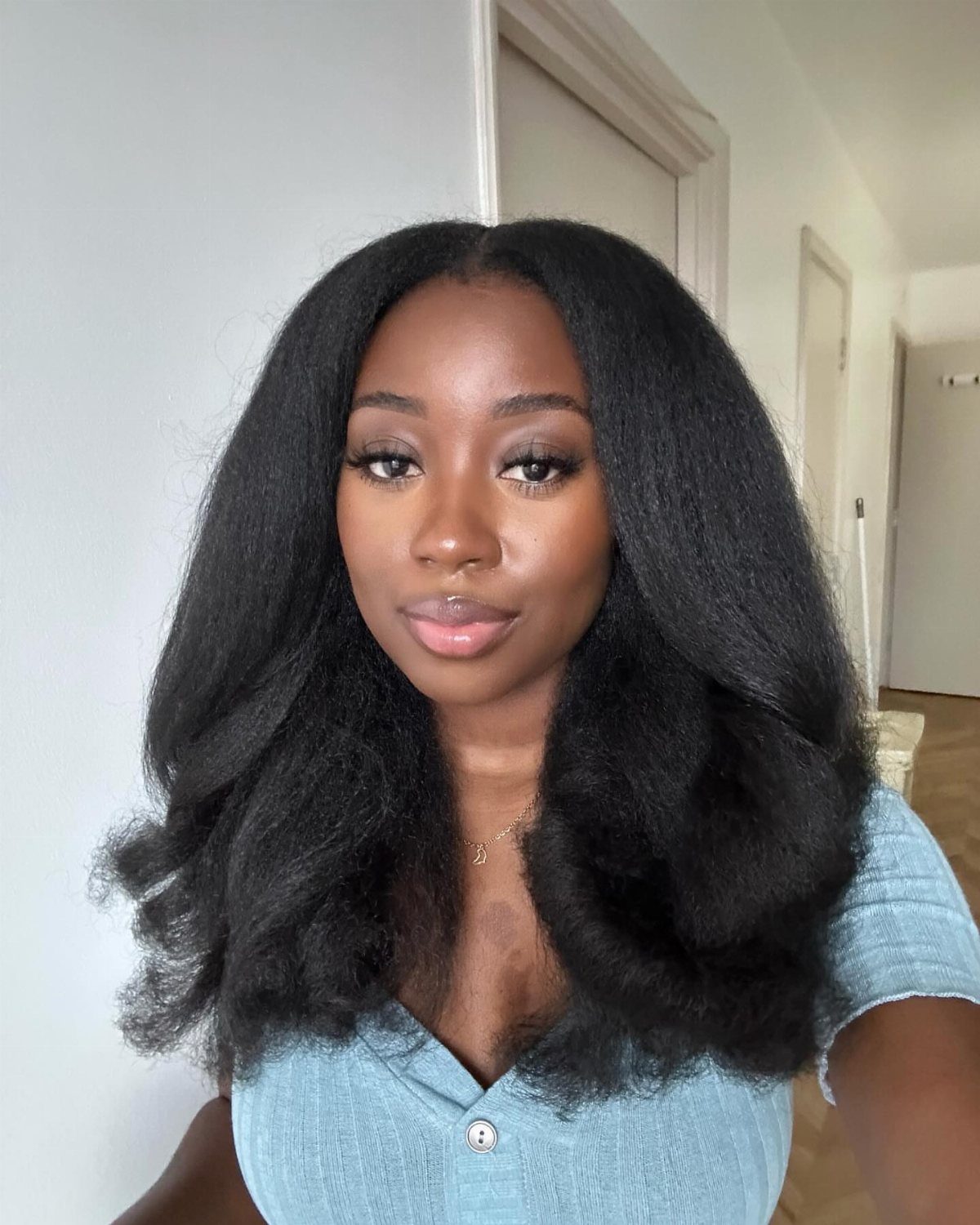 Woman with voluminous long black afro hair wearing a light blue ribbed top.