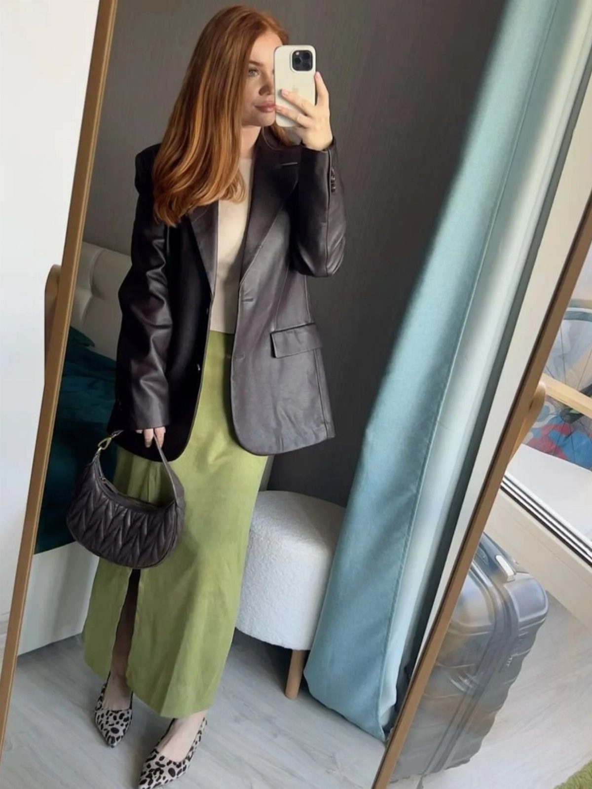 Woman in brown leather blazer and lime green skirt taking a mirror selfie
