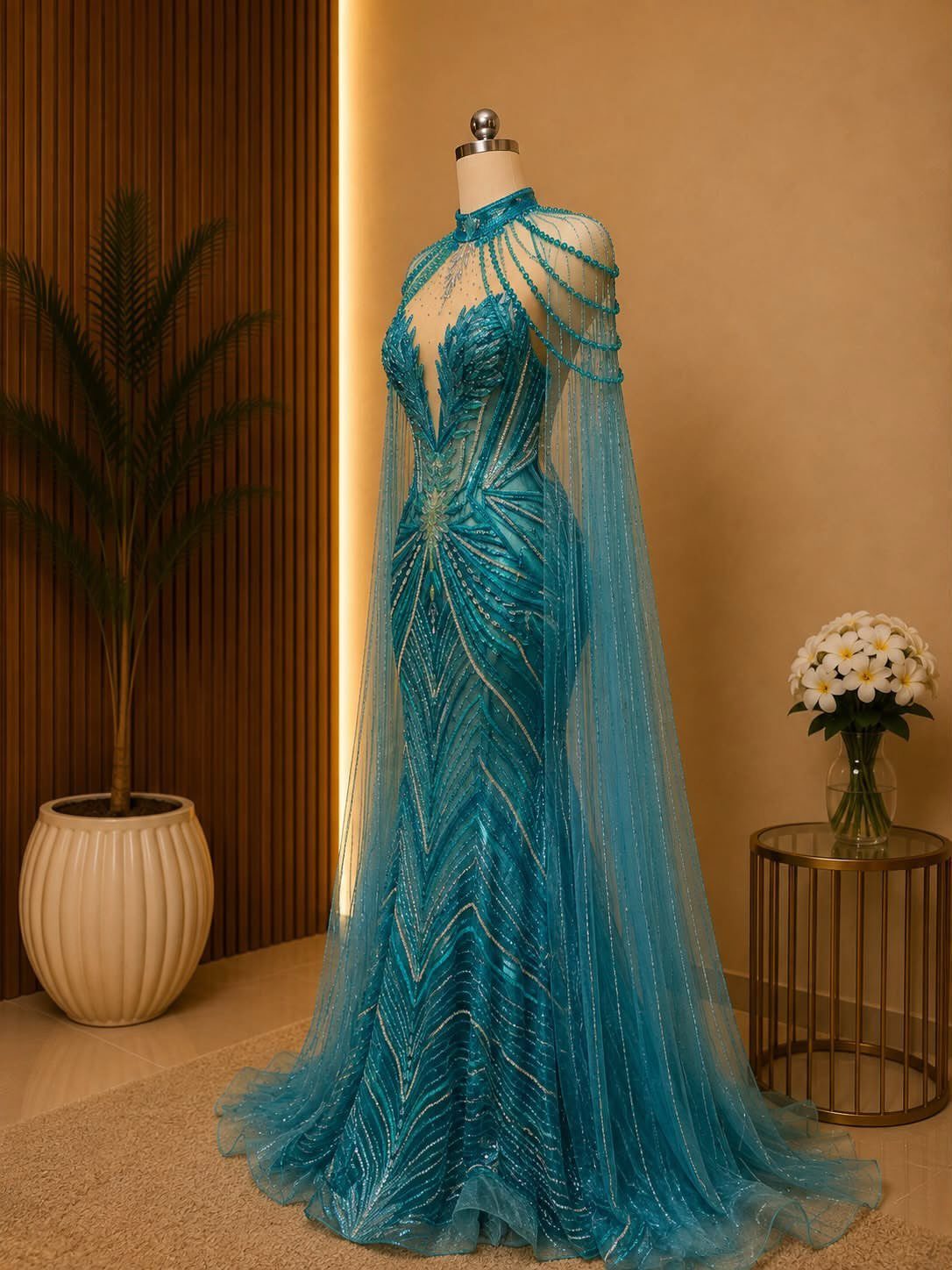 Teal-blue beaded mermaid gown with a sheer cape on a mannequin.