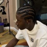 Man with cornrow braids in a barbershop wearing a white t-shirt and jeans