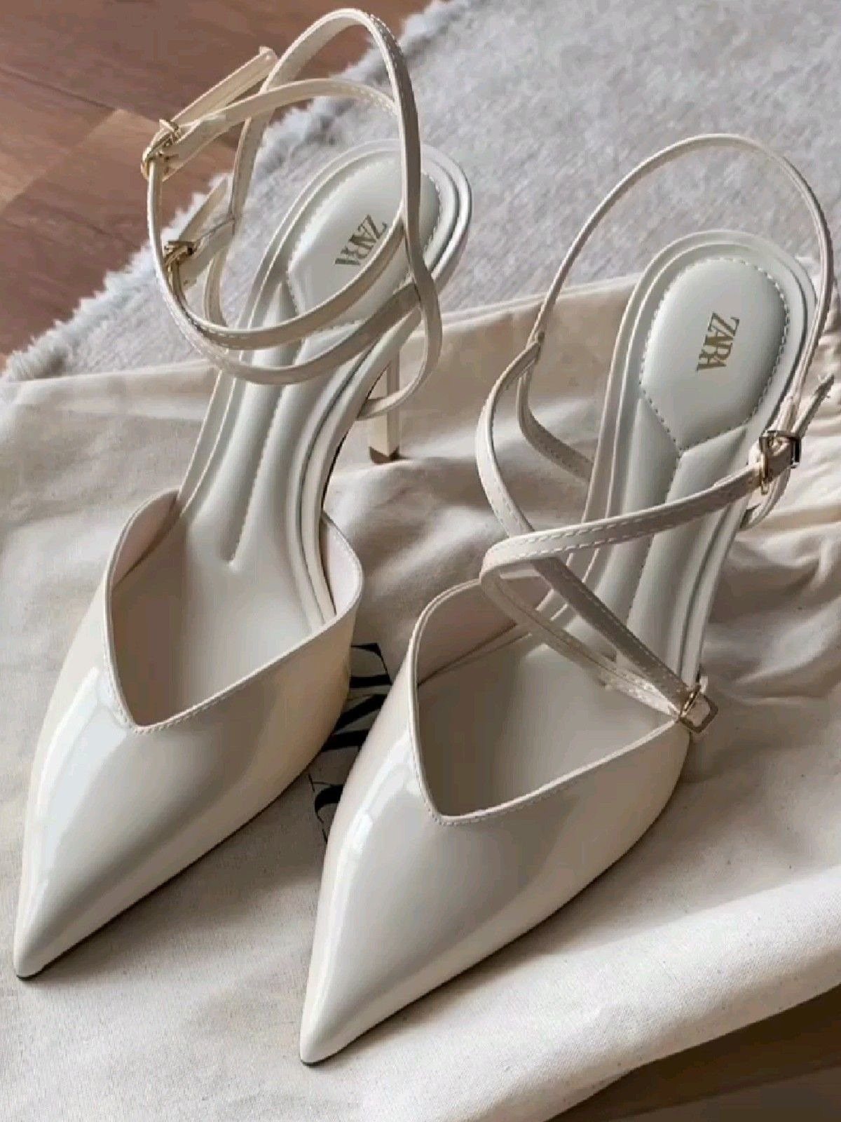 White pointed-toe high-heeled sandals with ankle straps on a white fabric surface.
