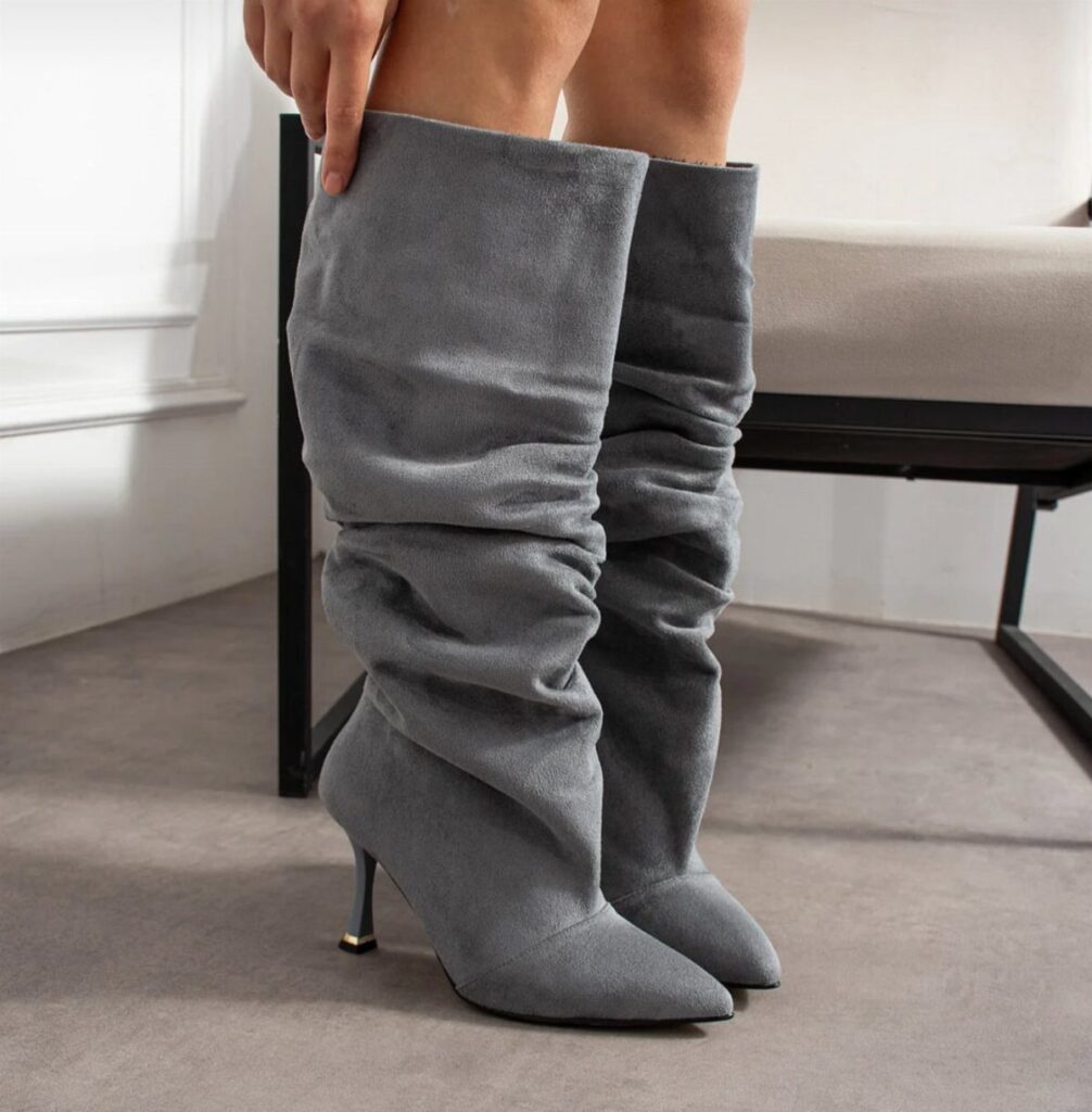 Grey slouchy knee-high suede boots with stiletto heels worn by a person.
