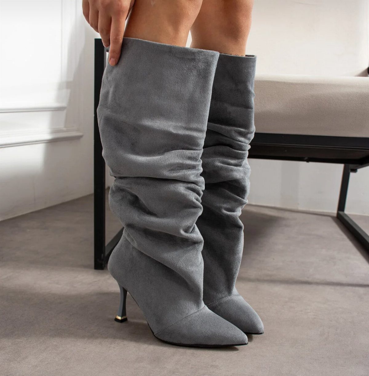 Grey slouchy knee-high suede boots with stiletto heels worn by a person.