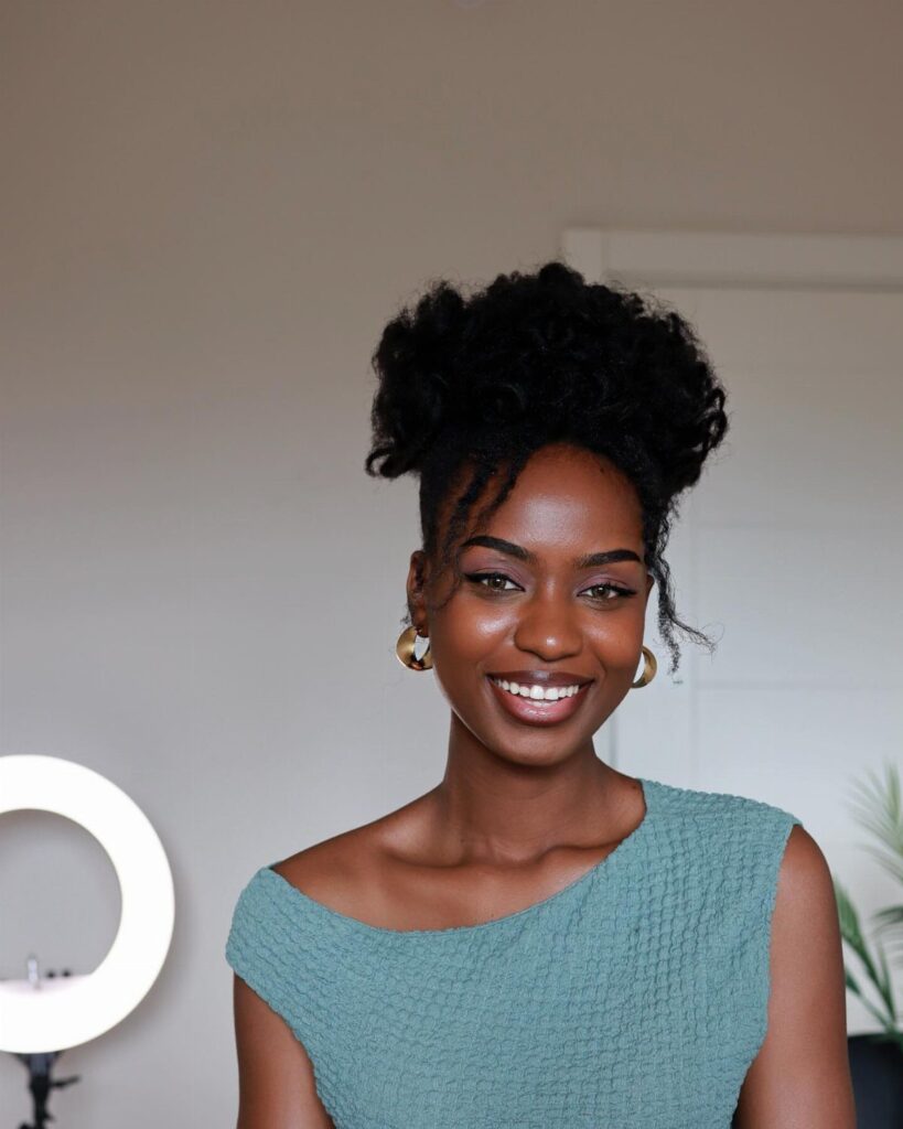Black woman with defined 4c curly hair styled in a high updo smiling