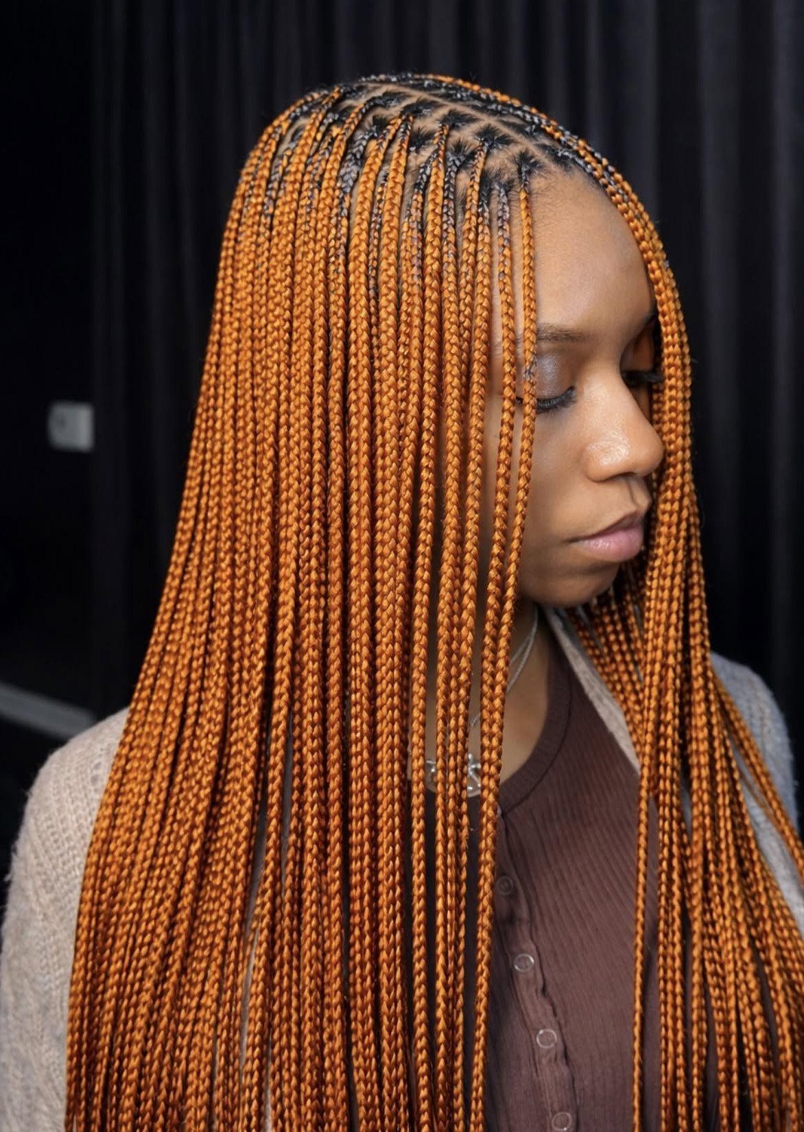 Woman with long copper-colored box braids and neat scalp parts against black background