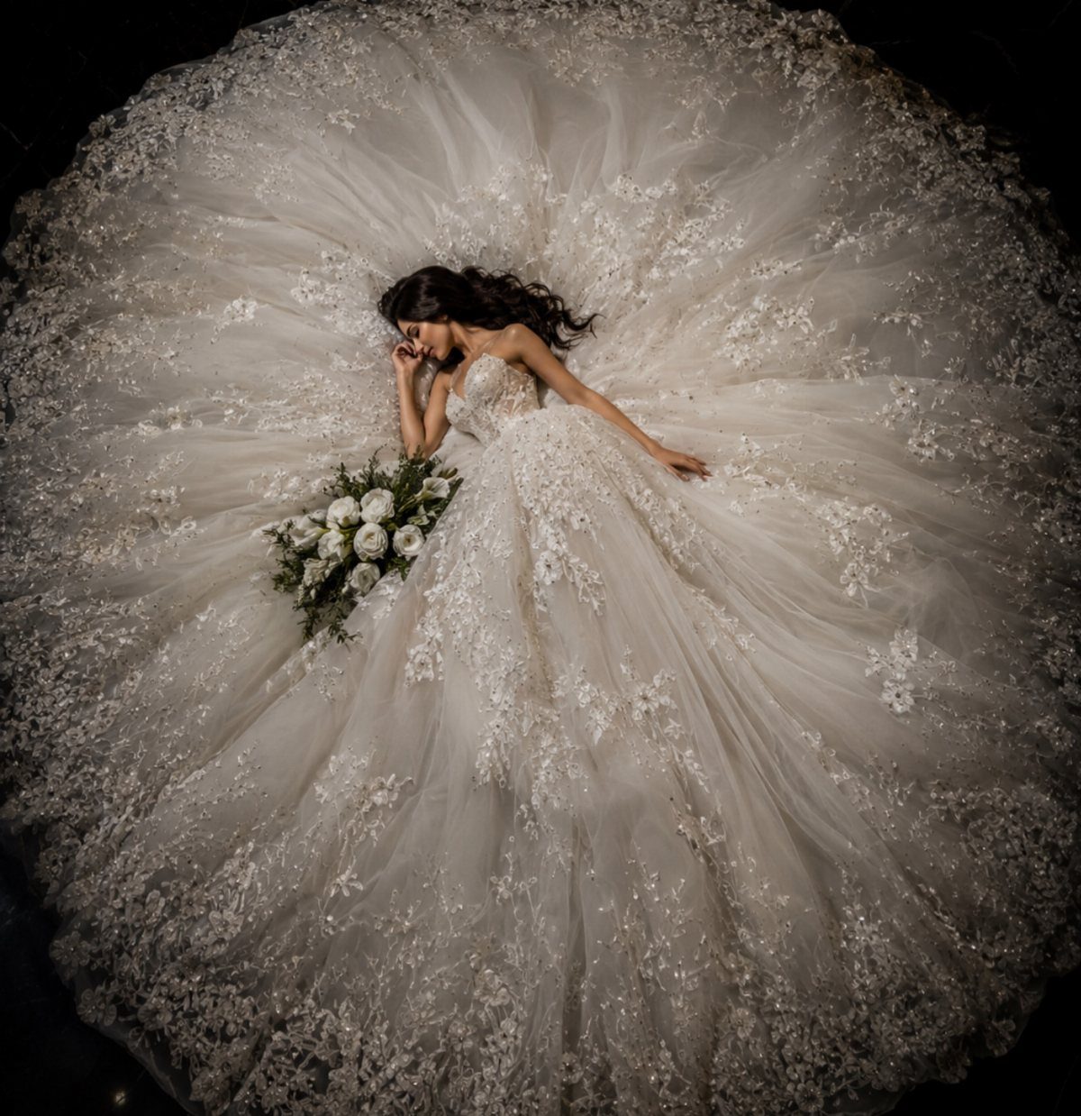 Woman in a voluminous white lace bridal gown lying with white roses