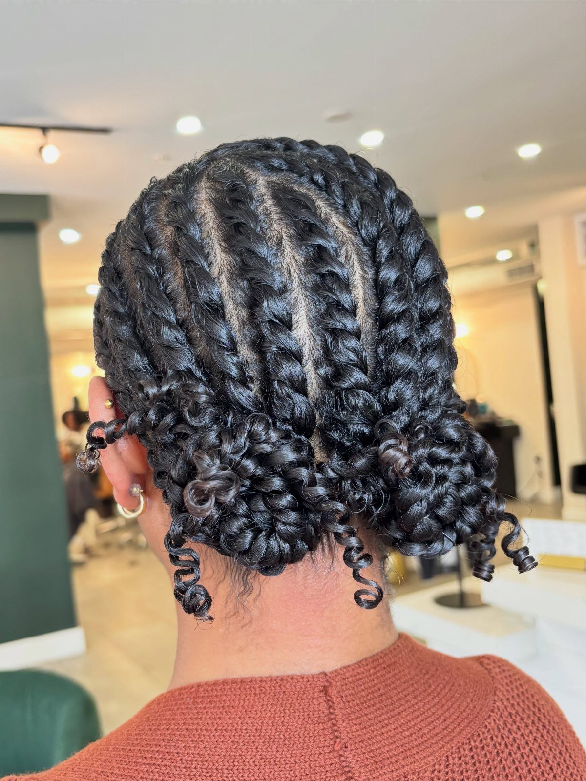 Black hair styled in flat twists leading into a curly updo at the nape.