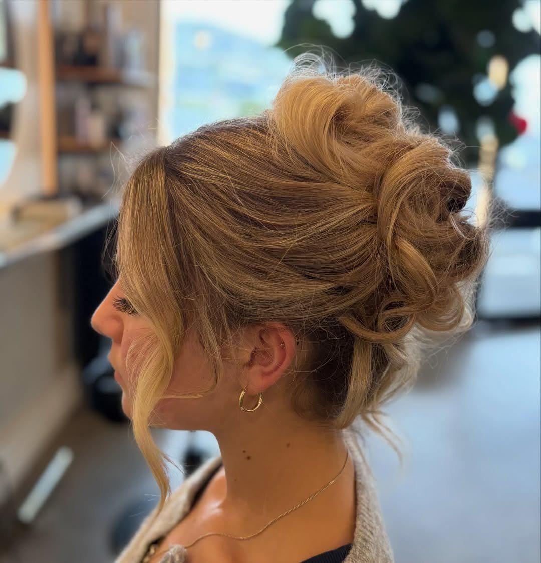 Woman with blonde hair styled in a voluminous, curly high updo for a ball.