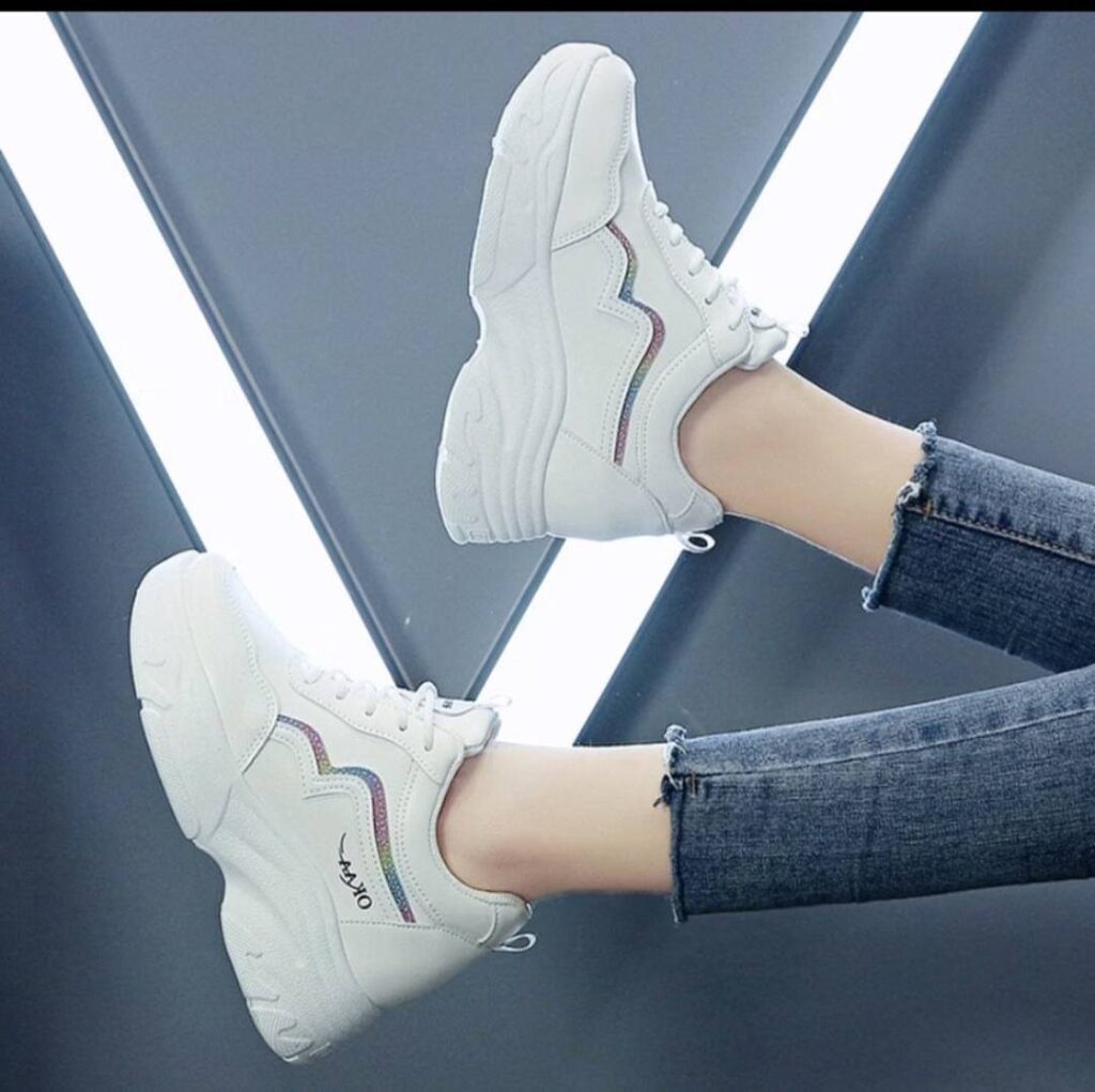 White hidden wedge sneakers with rainbow accents worn with blue denim jeans.