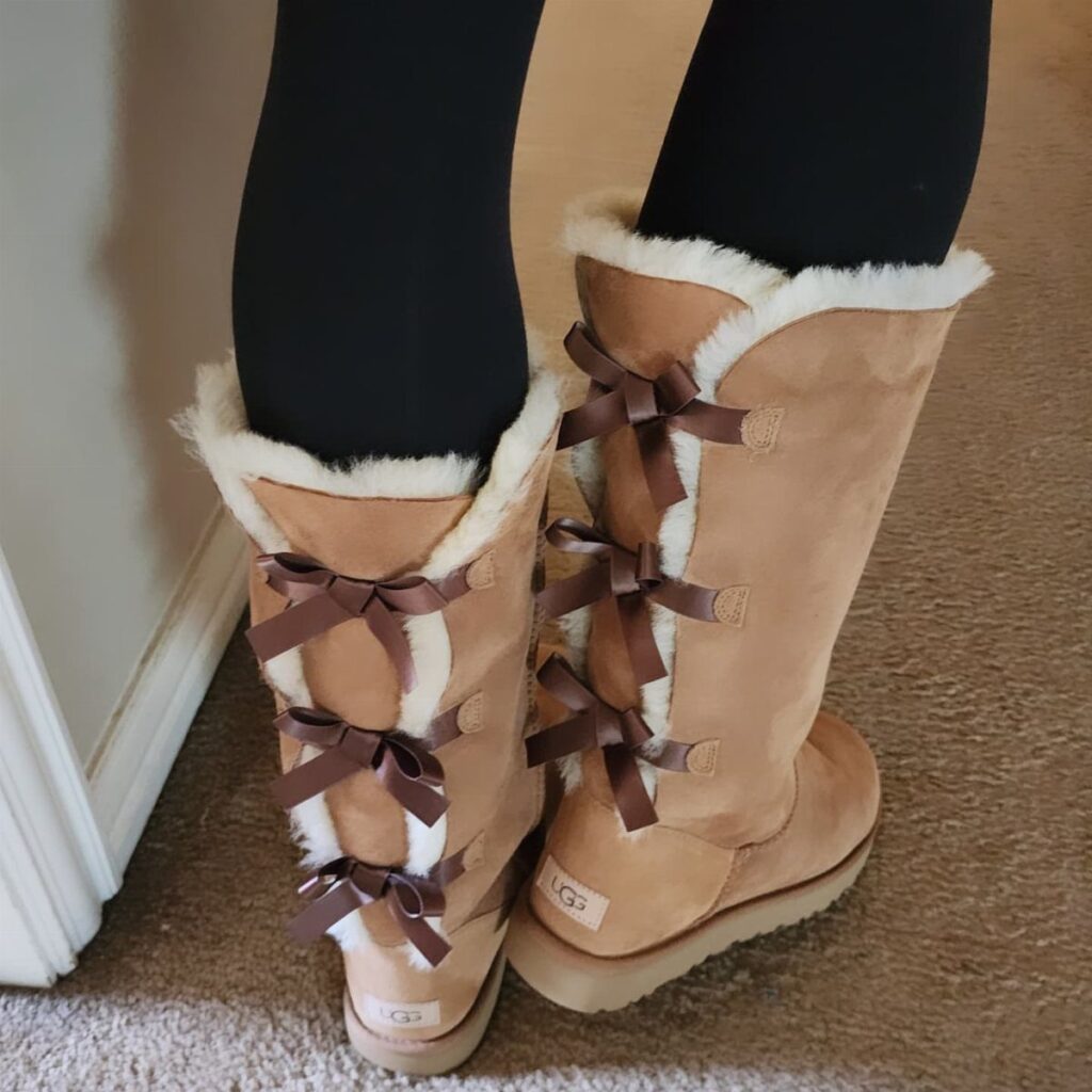 Tall tan suede UGG boots with brown ribbon bows and white fur trim.