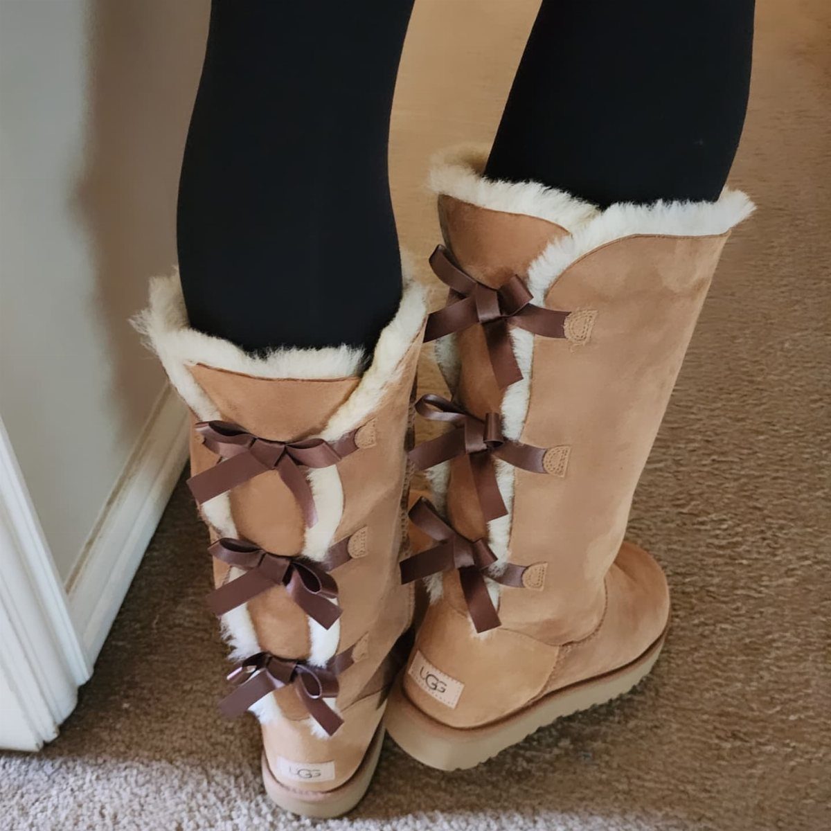 Tall tan suede UGG boots with brown ribbon bows and white fur trim.