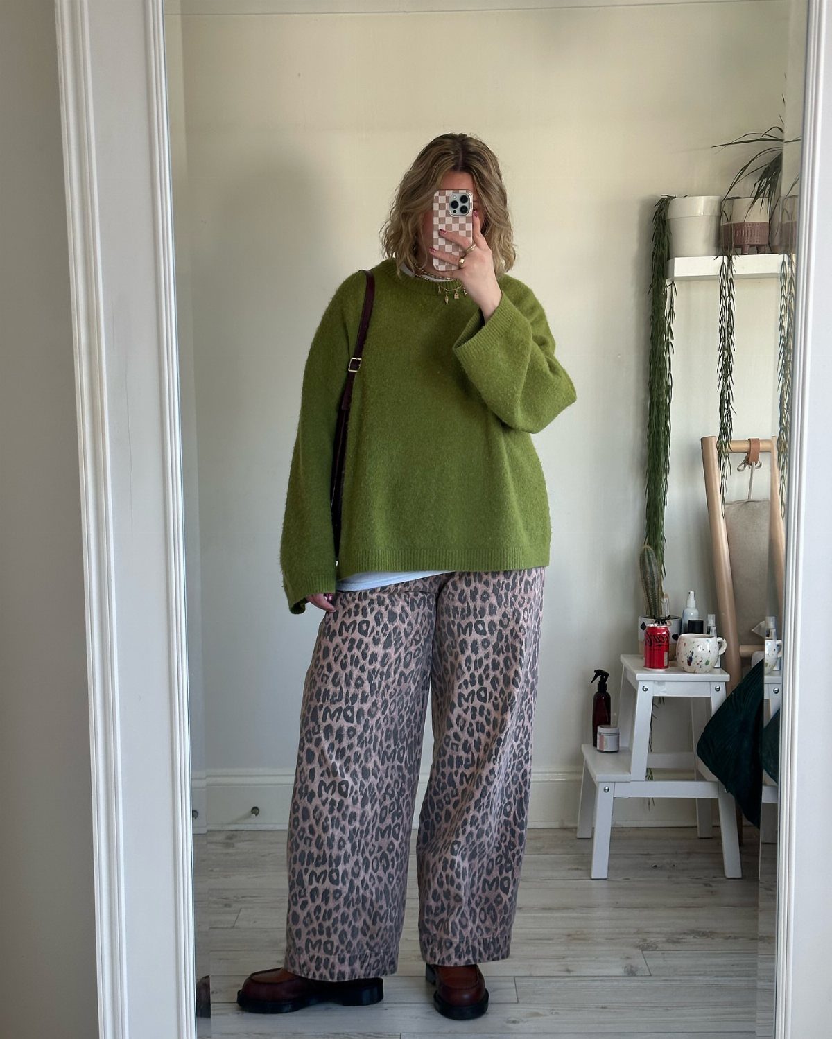 Person in a green sweater and leopard print wide-leg pants taking a mirror selfie.