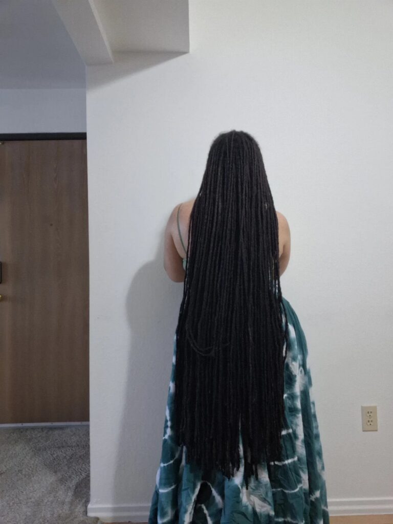 Person from behind with very long black dreadlocks and tie-dye clothing