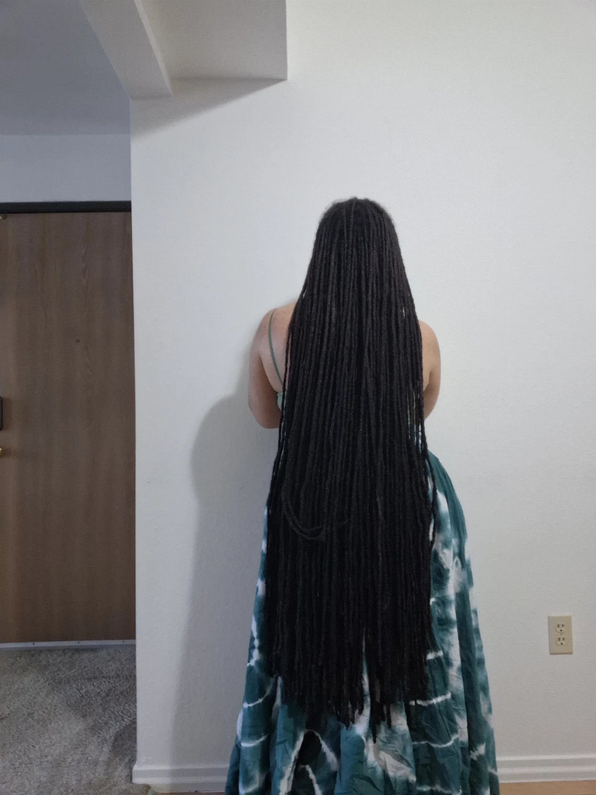 Person from behind with very long black dreadlocks and tie-dye clothing