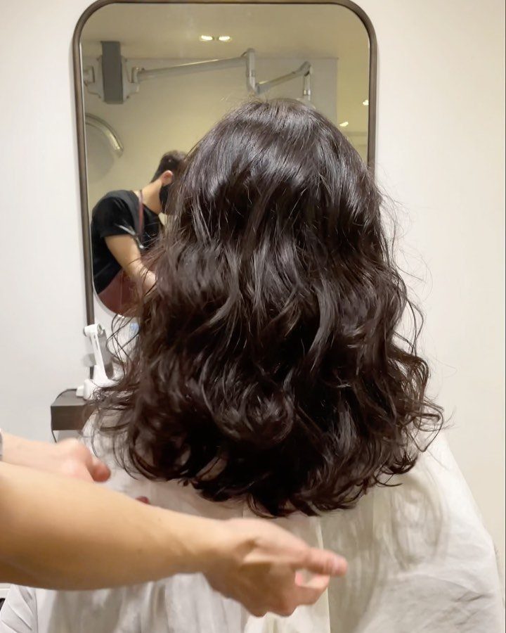 Medium length dark brown permed hair with voluminous curls in a salon setting