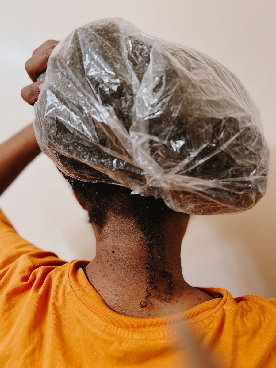 Person with curly hair wearing a clear plastic shower cap and orange shirt.