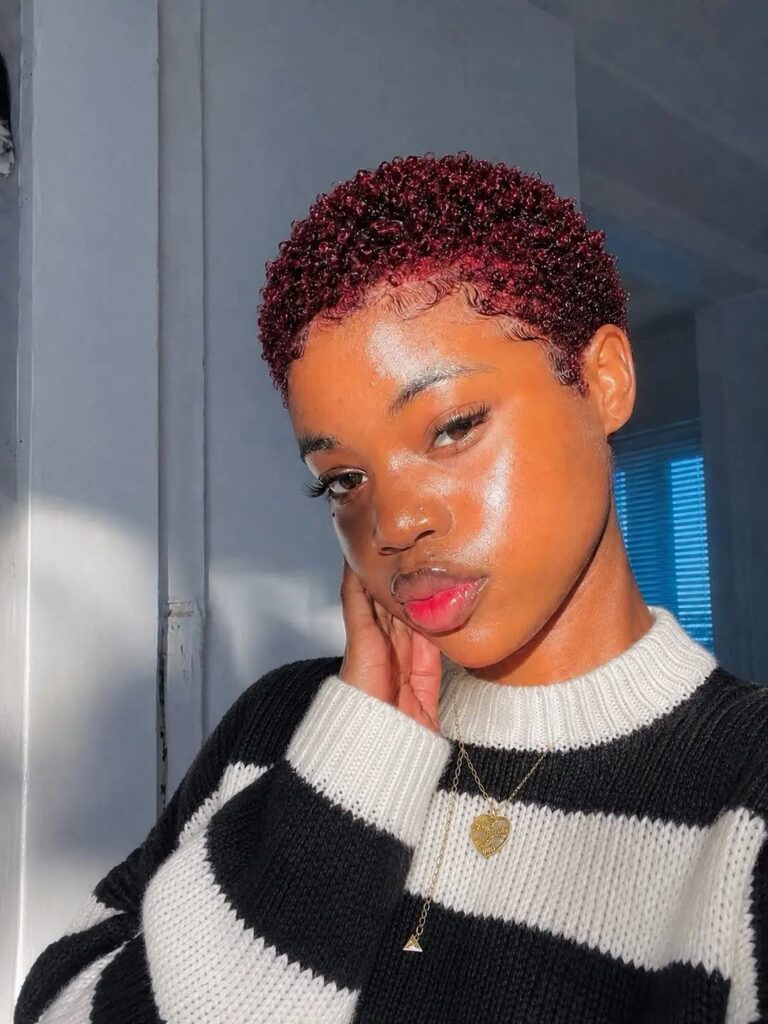 Woman with short curly reddish-brown natural hair wearing a striped sweater and necklace.