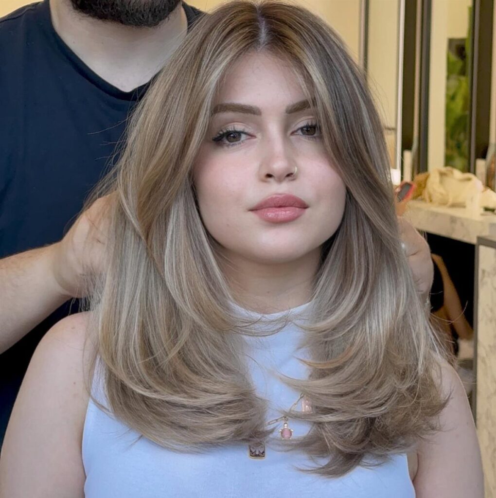 Woman with long, layered ash-blonde hair and subtle highlights in a salon setting
