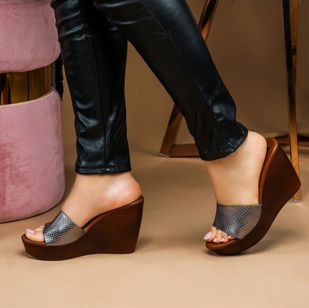 Brown wooden wedge sandals with silver straps worn with black leather pants.