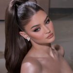 Woman with a sleek high ponytail and white flower earrings posing for a portrait.