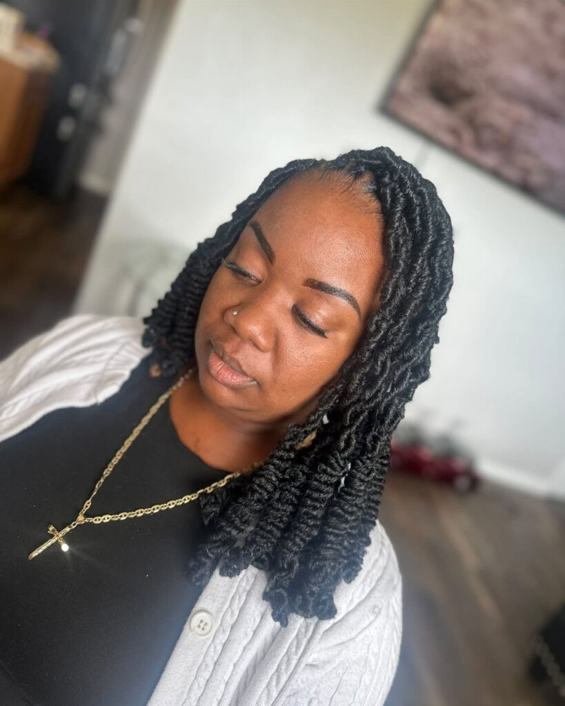 Woman with shoulder-length black faux locs wearing a white cardigan and gold necklace.