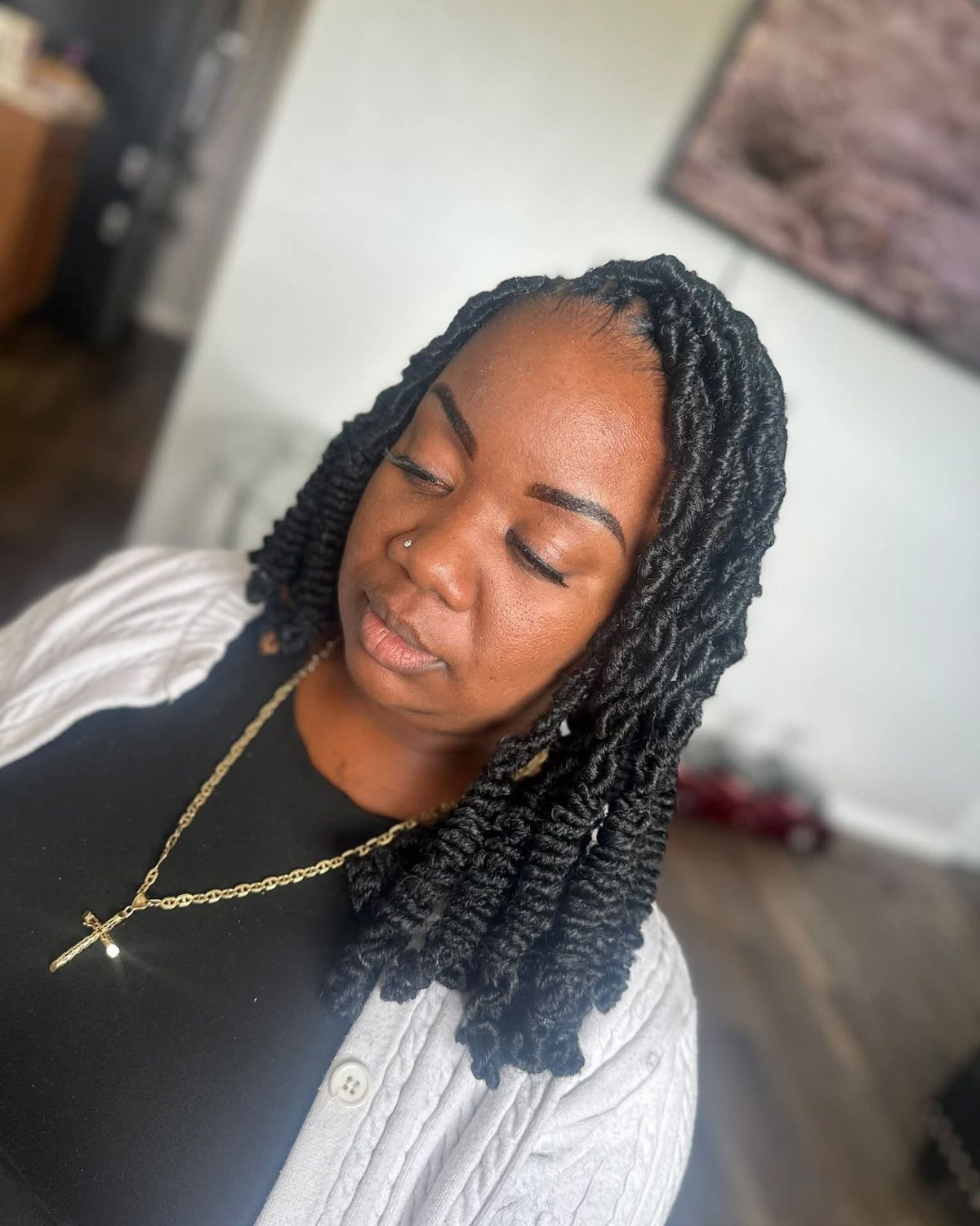 Woman with shoulder-length black faux locs wearing a white cardigan and gold necklace.