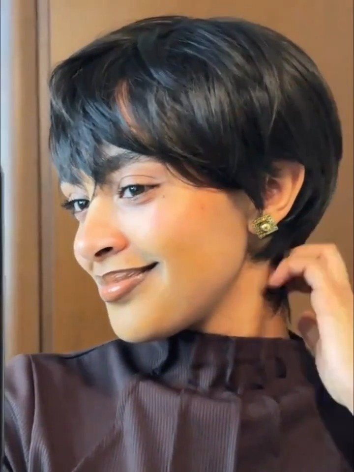 Person wearing a short black pixie-cut wig and gold earrings posing for camera