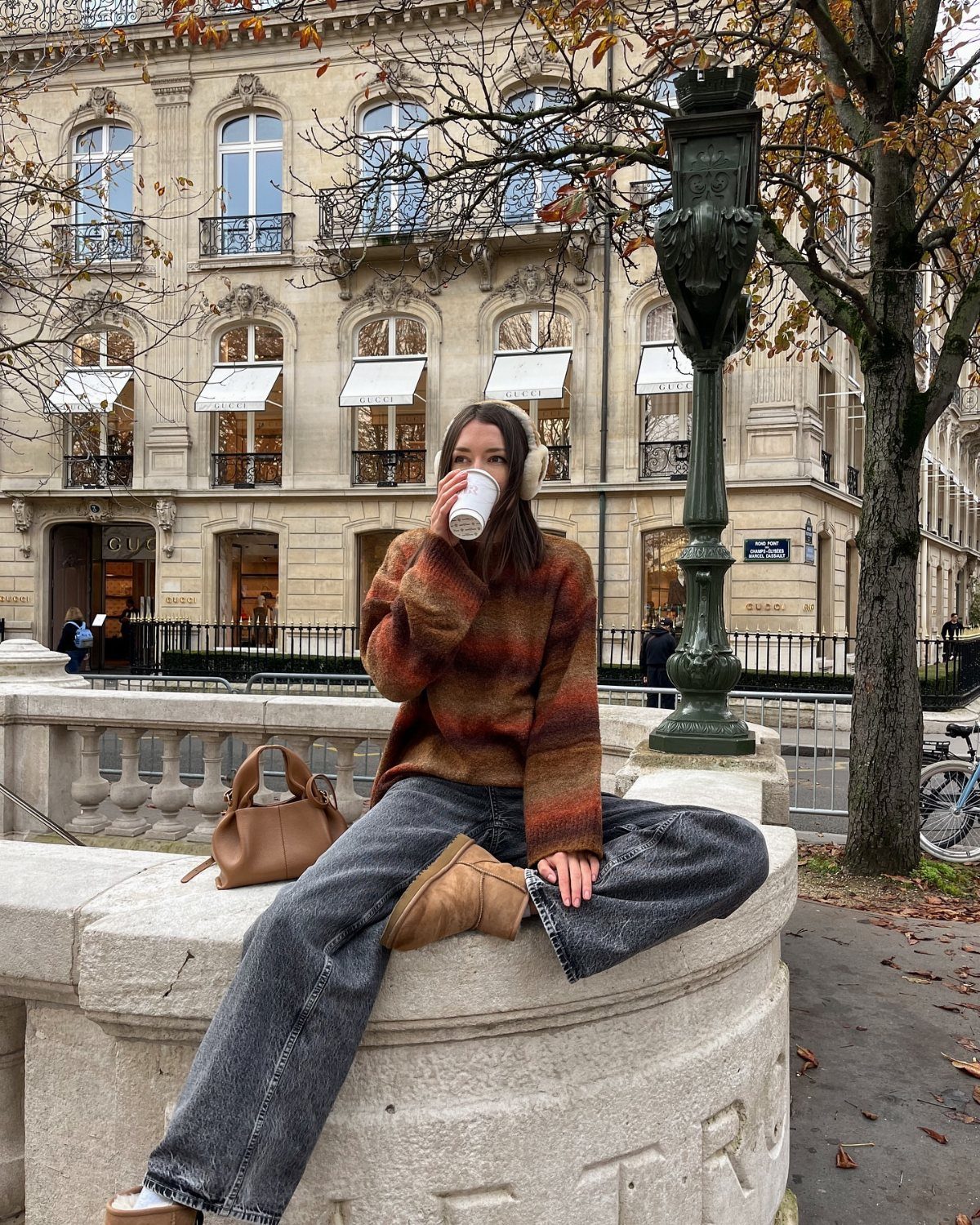 Woman wearing chestnut short UGG boots, grey jeans, and a striped sweater sitting outdoors.