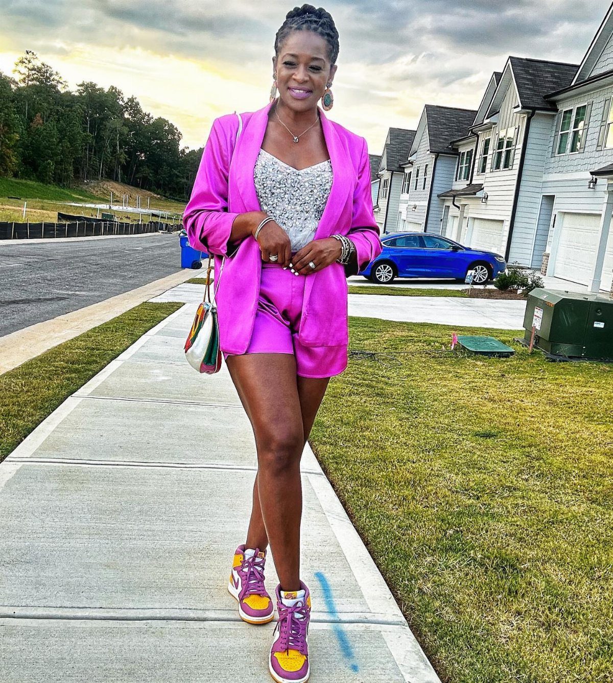 Woman in pink blazer and shorts wearing purple and yellow sneakers on sidewalk