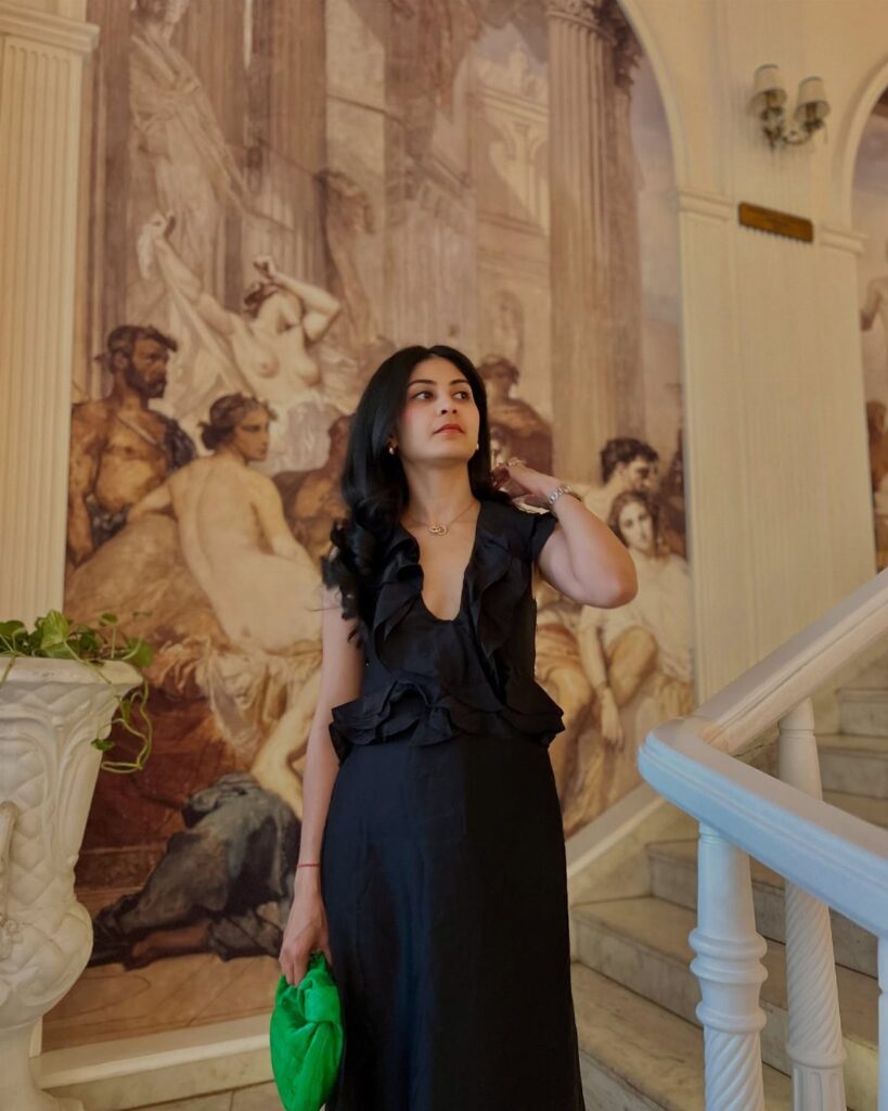Woman in a black ruffled maxi dress holding a green clutch by a mural