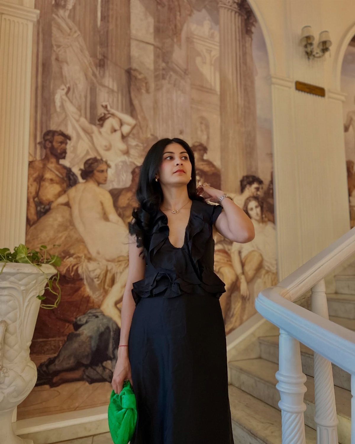 Woman in a black ruffled maxi dress holding a green clutch by a mural
