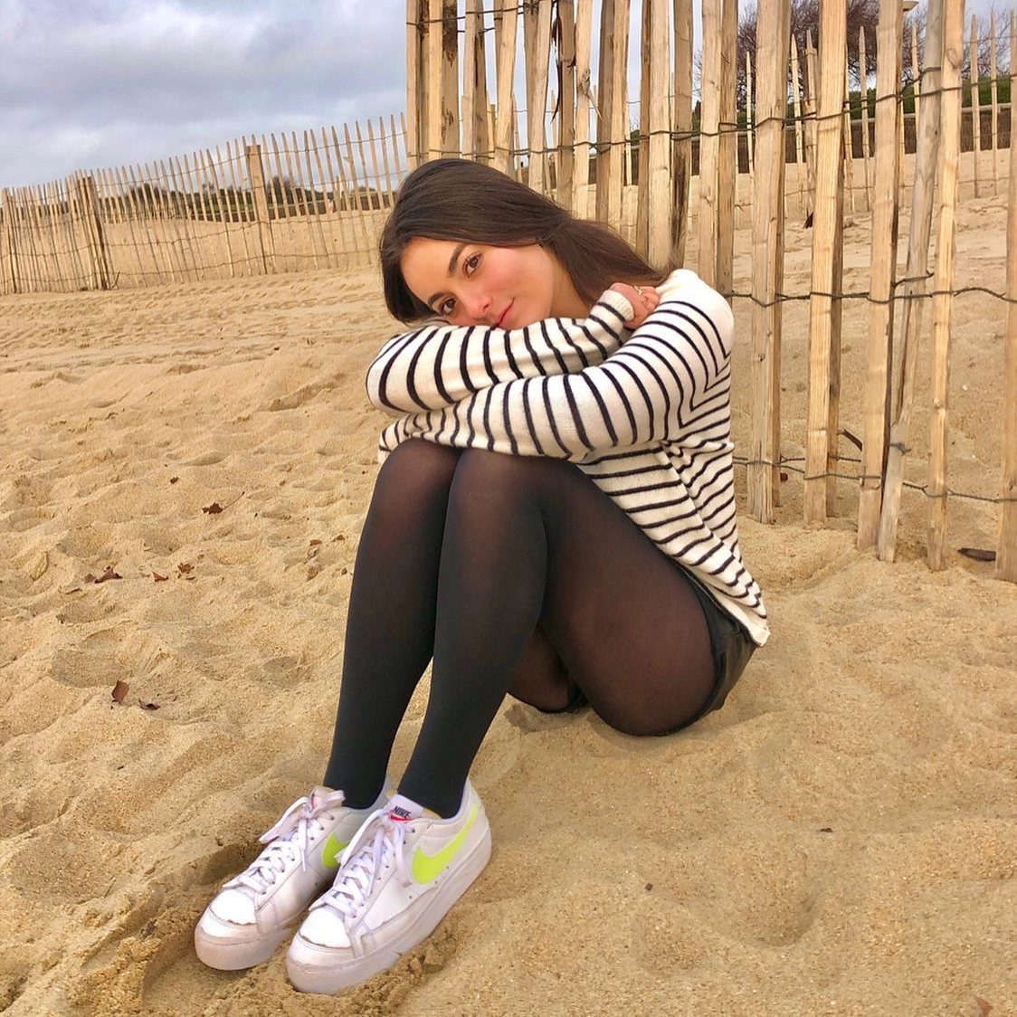 Woman in striped shirt and black tights sitting on a sandy beach