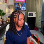 Woman with two strand twist hairstyle wearing a navy blue t-shirt and gold chain.