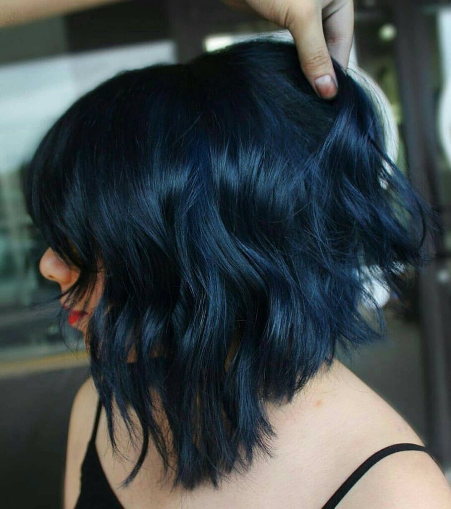 Wavy shoulder-length hair dyed a deep blue-black color held by a hand.