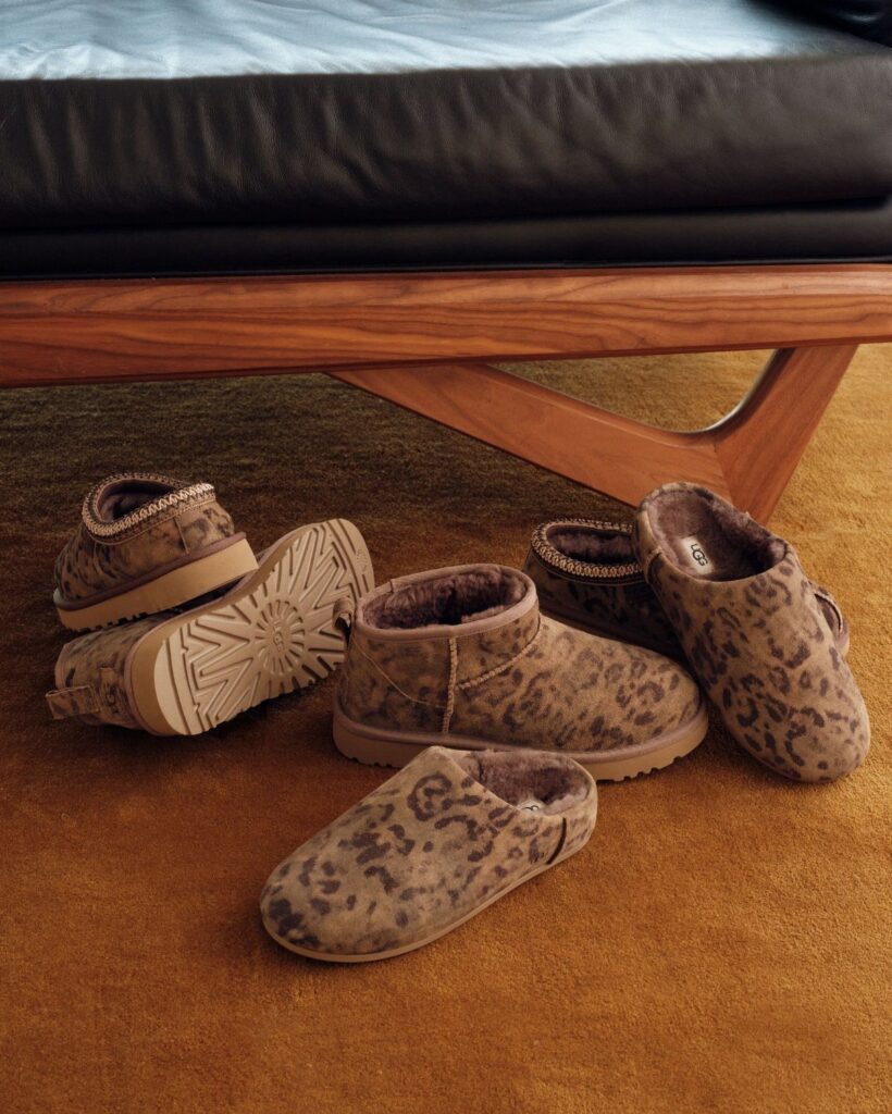 Leopard print sheepskin boots and slippers arranged on a brown carpeted floor.
