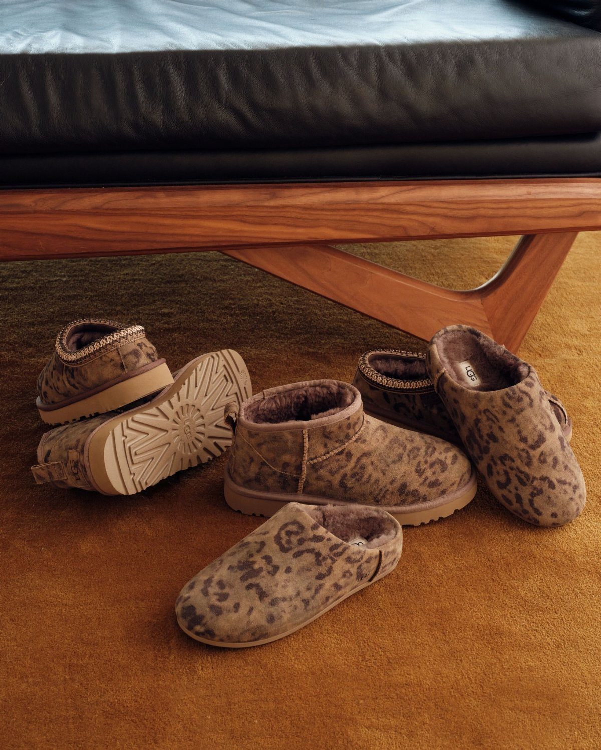 Leopard print sheepskin boots and slippers arranged on a brown carpeted floor.