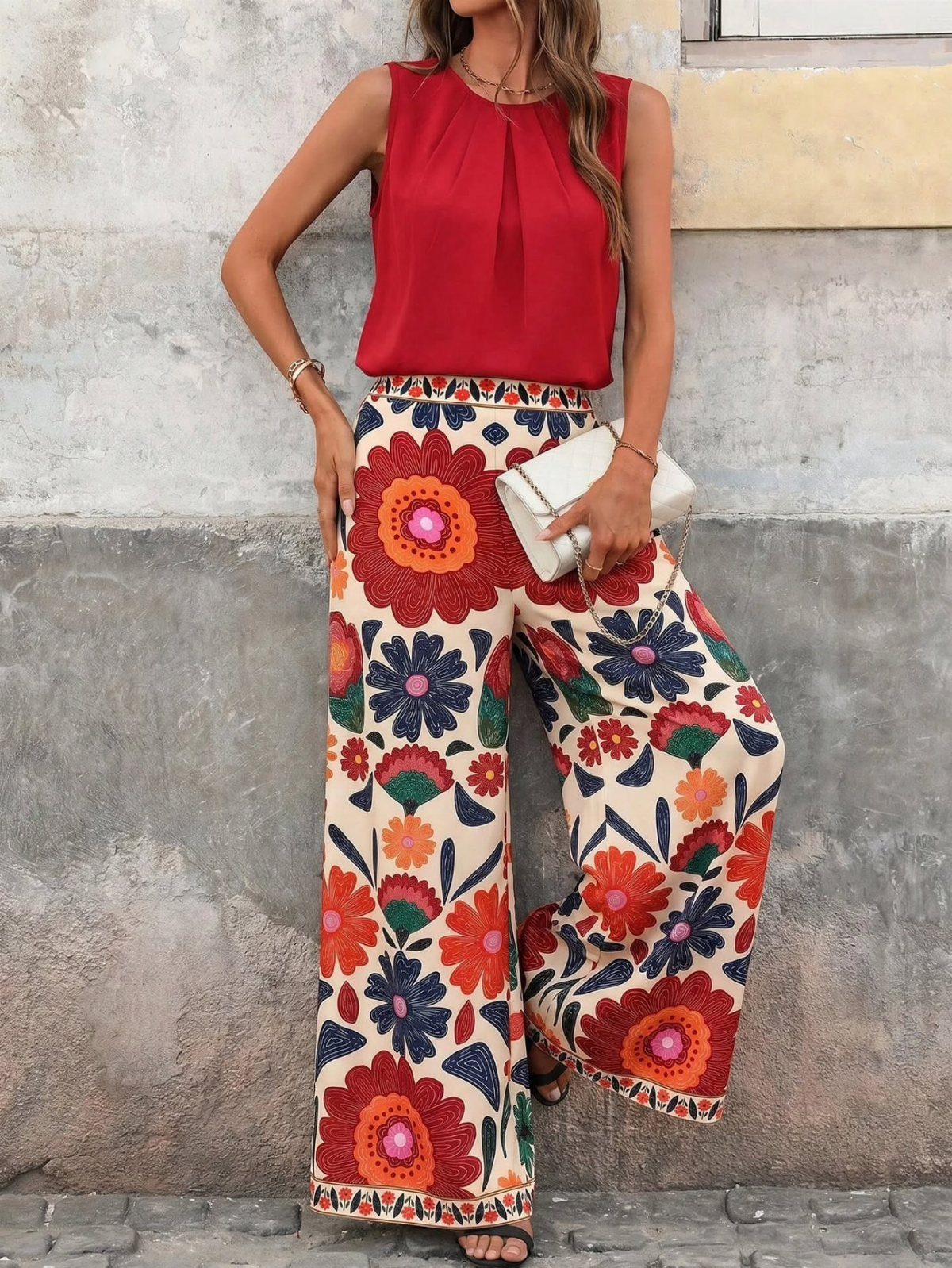 Woman wearing a red sleeveless top and colorful floral wide-leg trousers with white clutch.