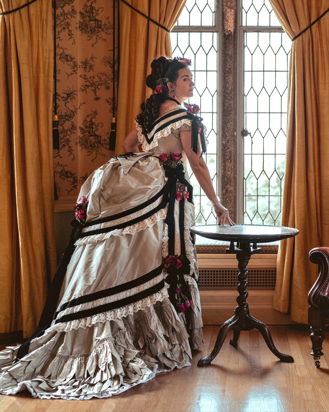 Woman in a champagne Victorian ball gown with black ribbons by a window
